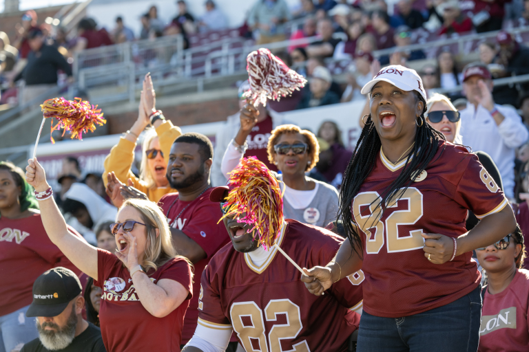 Elon fans cheer enthusiastically from the stands, waving pom-poms during a home football game.