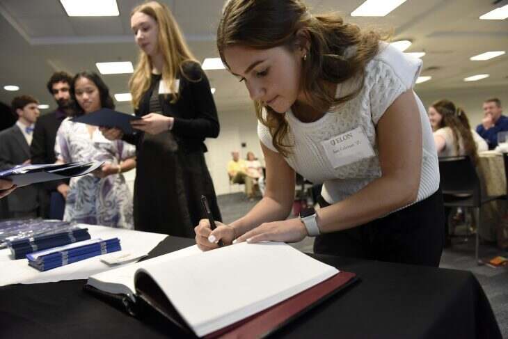 Female with brown hair and wearing a white blouse writing her signature at the Phi Beta Kappa induction.