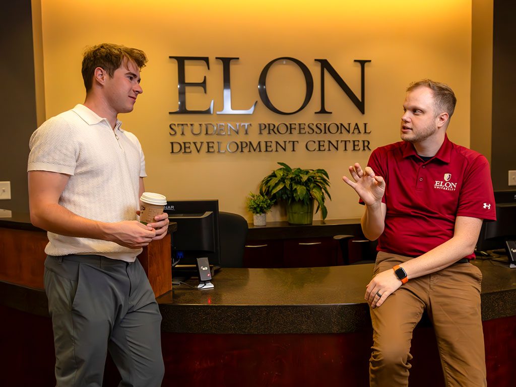 photo of a student and staff member chatting at the front desk of the Elon Student Professional Development Center