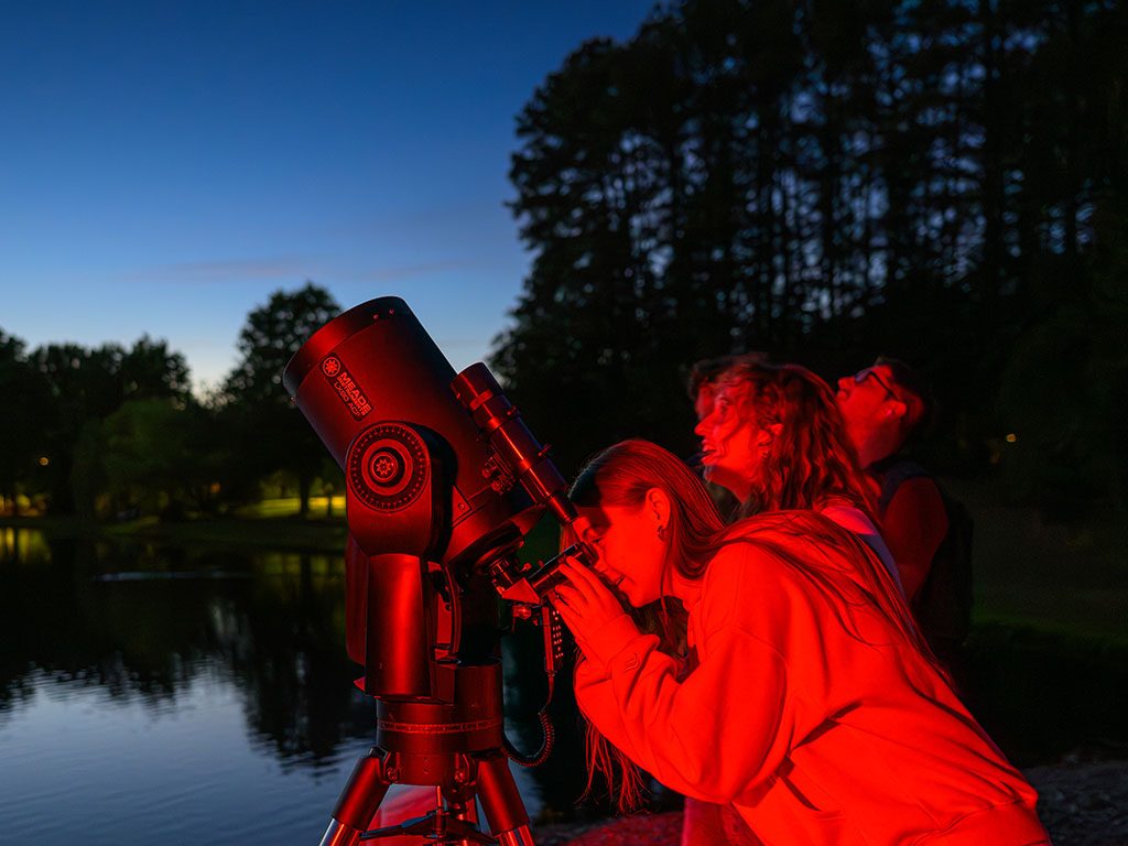 Photo of students using a telescope to observe the night sky beside Lake mary Nell during the Stargazing for Mental Health event