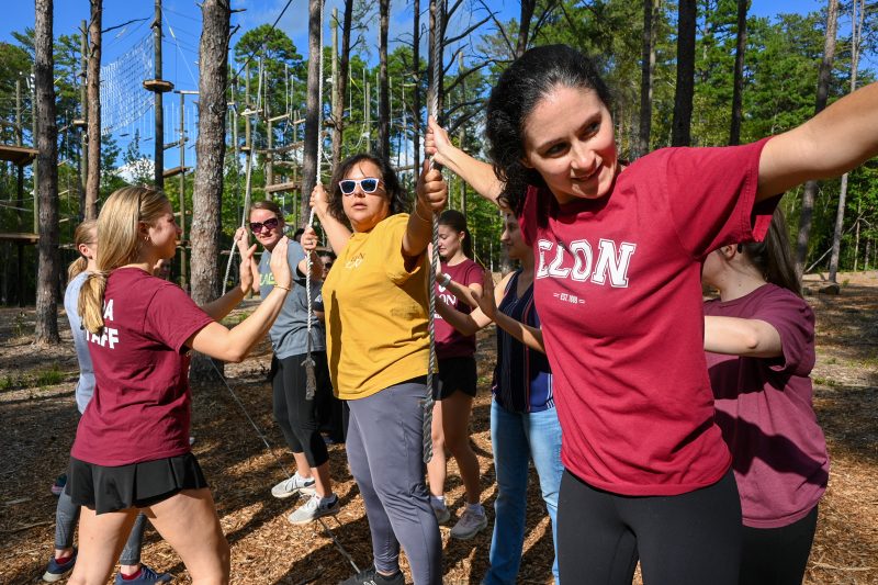 Elon University faculty and staff navigating a low ropes course team-building activity during a Together@Elon event, balancing and supporting each other outdoors.