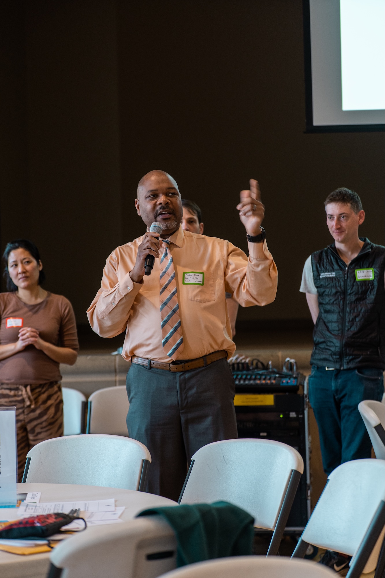 a community member holding a microphone speaks while other community members watch and listen