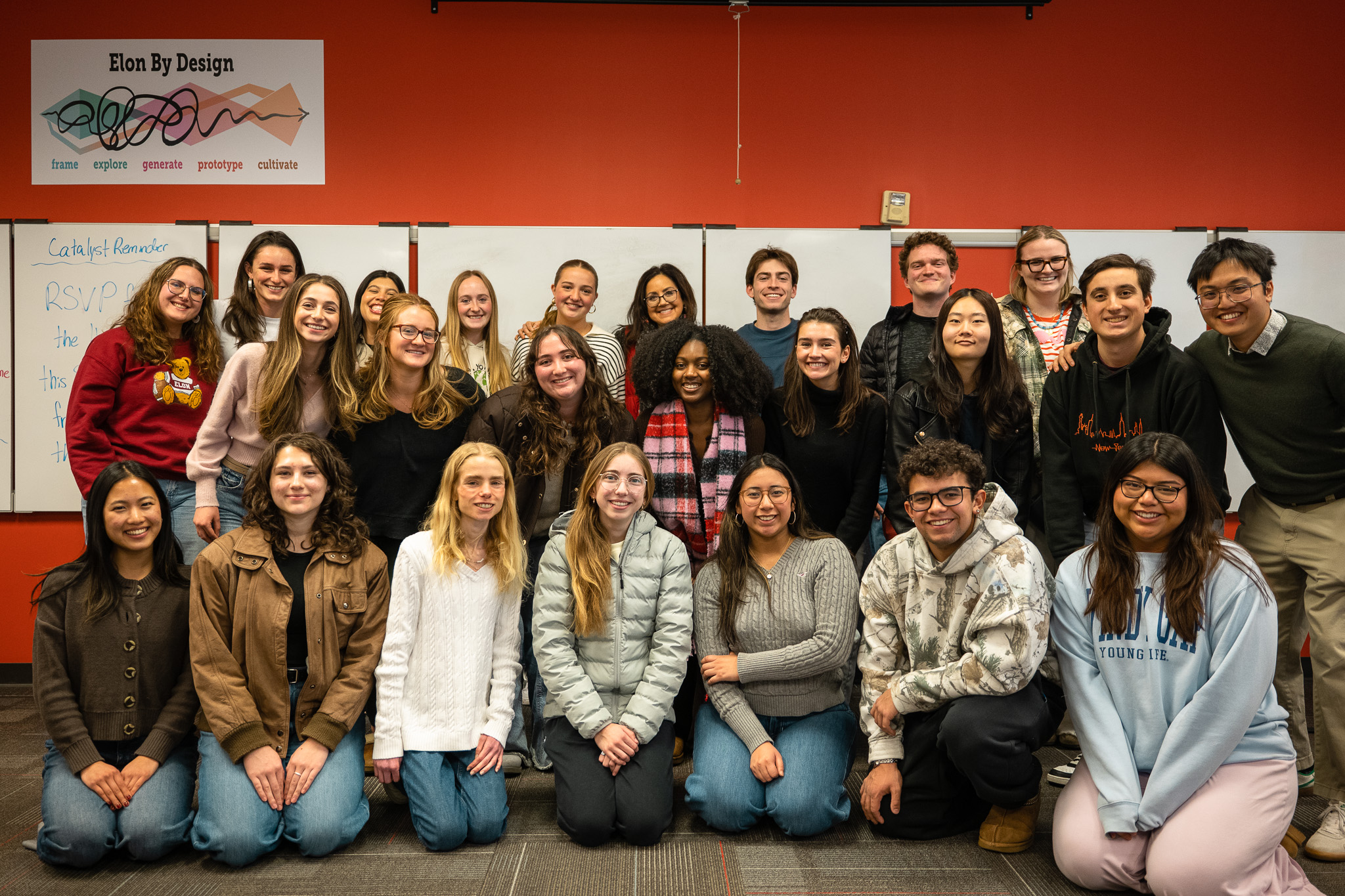 a group of 23 students and center for design thinking director danielle lake posing for a group photo at the front of the design thinking classroom space