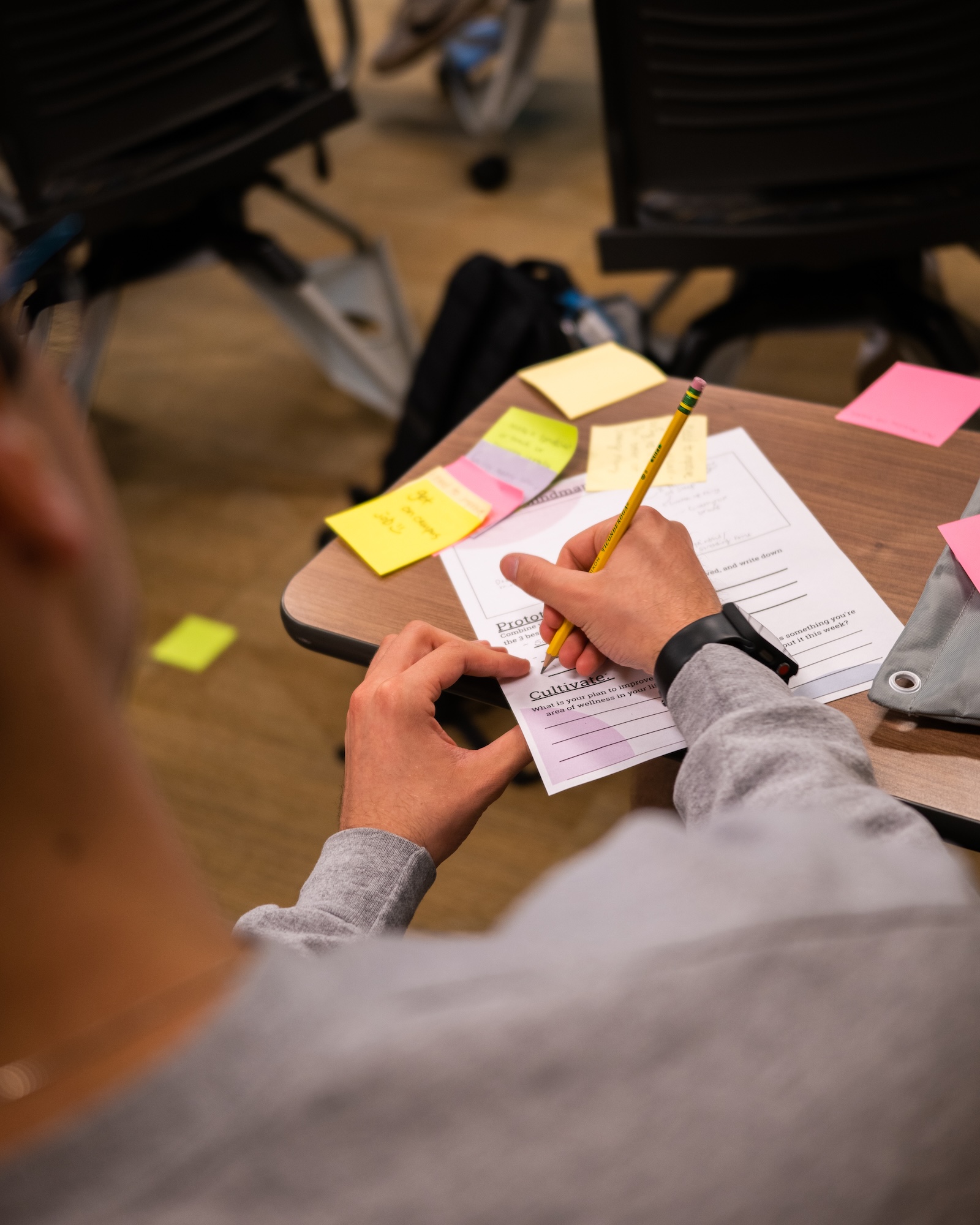 an over-the-shoulder point of view of a workshop participant using a pencil to fill out a design thinking worksheet