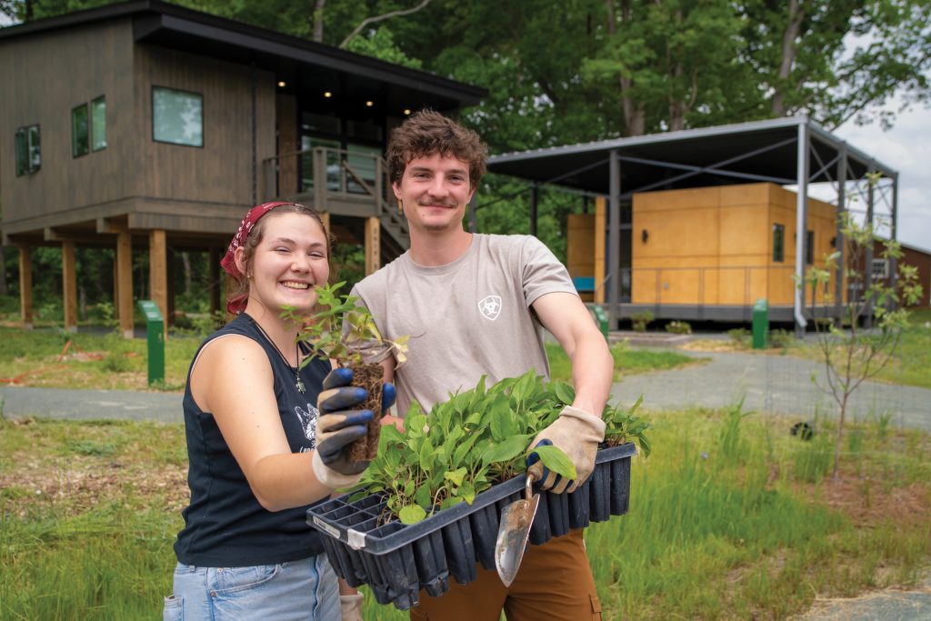 Two students smile as they hold seedlings they are about to plant at Elon University's Eco Village neighborhood