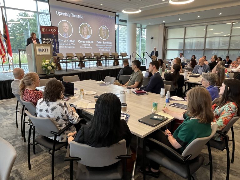 people sit at tables in a conference room listening to elon president connie book speak from a podium