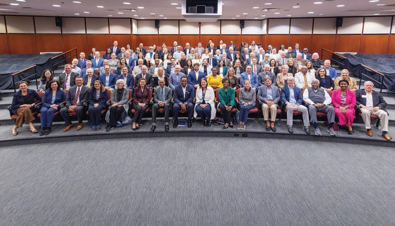 a large group photo of representatives from queens and elon universities sitting in a theatre