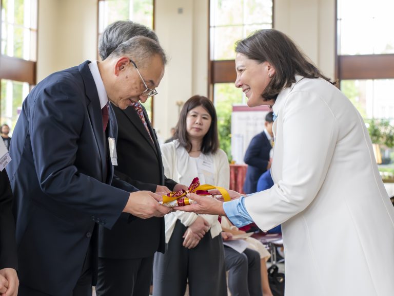 elon president connie book presents a gift wrapped package to one of japanese alum Toshio Sato’s decendents