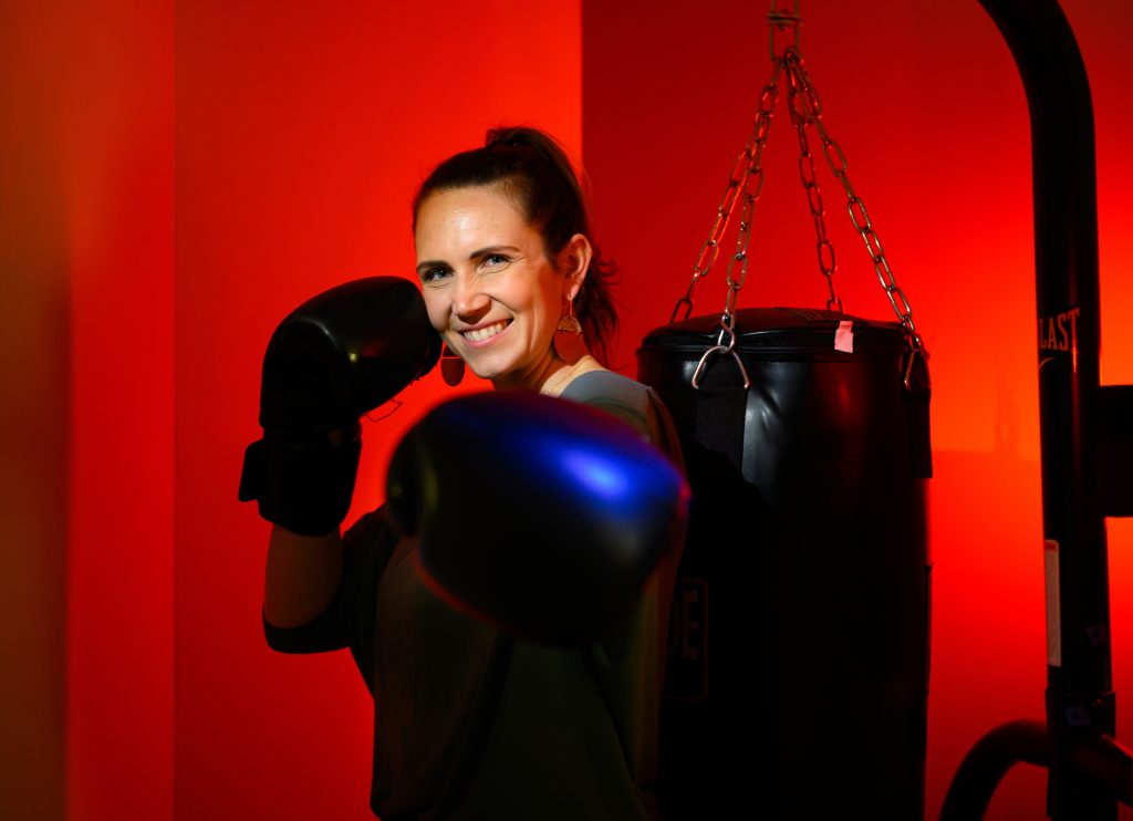 Woman wearing boxing gloves posing in front of a punching bag