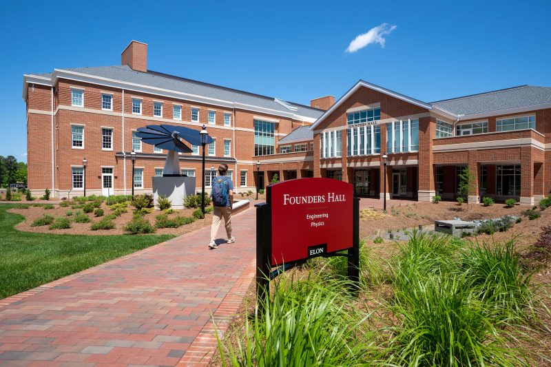 A student walks on a brick path toward Founders Hall