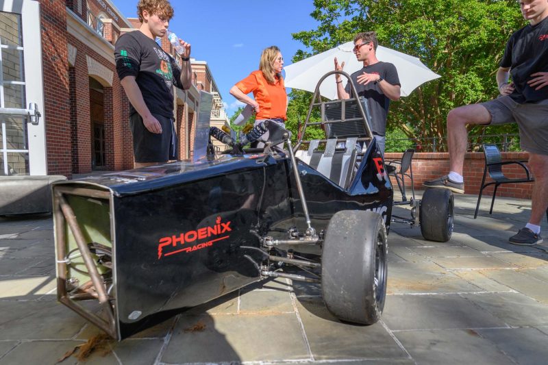 Members of the Phoenix Racing team talk with Maker takeover visitors in front of their electric F1 car