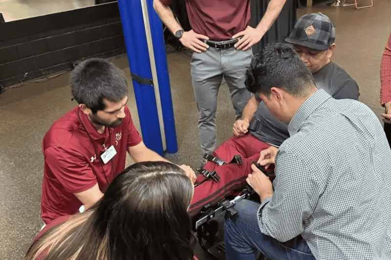 Students adjust straps around a man's legs on brace for walking with spinal disorder