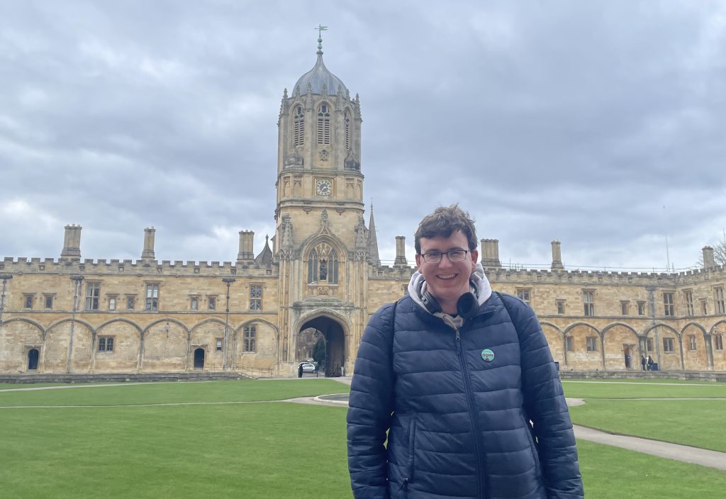 Jake Dyer smiles in Tom Quad at Christ Church, University of Oxford, with the historic Tom Tower behind him.
