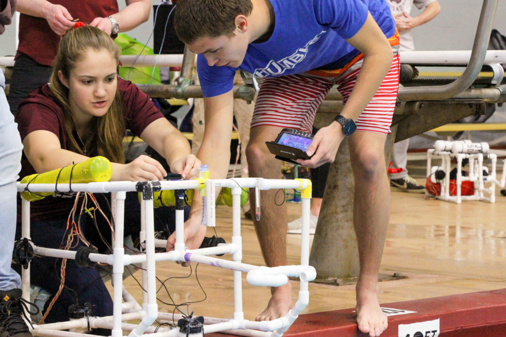 Student lean over connected pvc pipes at a pool as part of the Grand Challenges in Engineering course