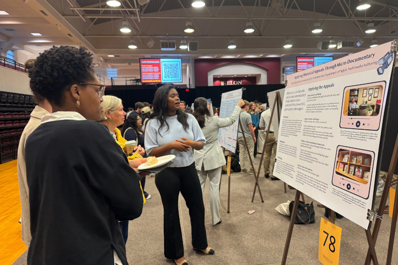 Student shares a project poster with onlooker