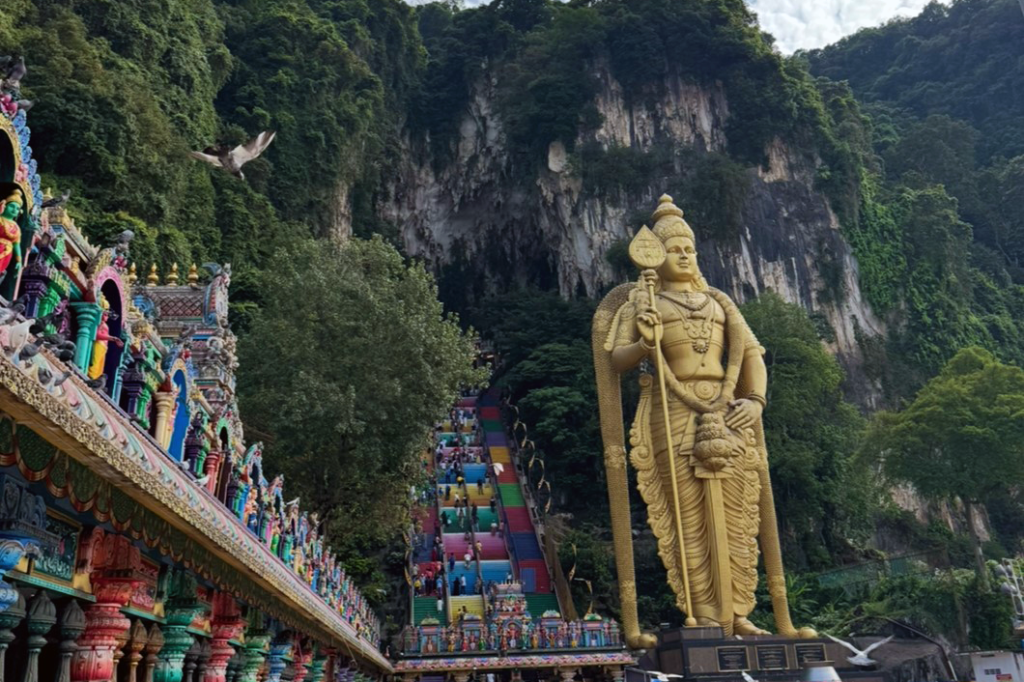Batu Caves in Malaysia, featuring the large golden Murugan statue and colorful staircase.