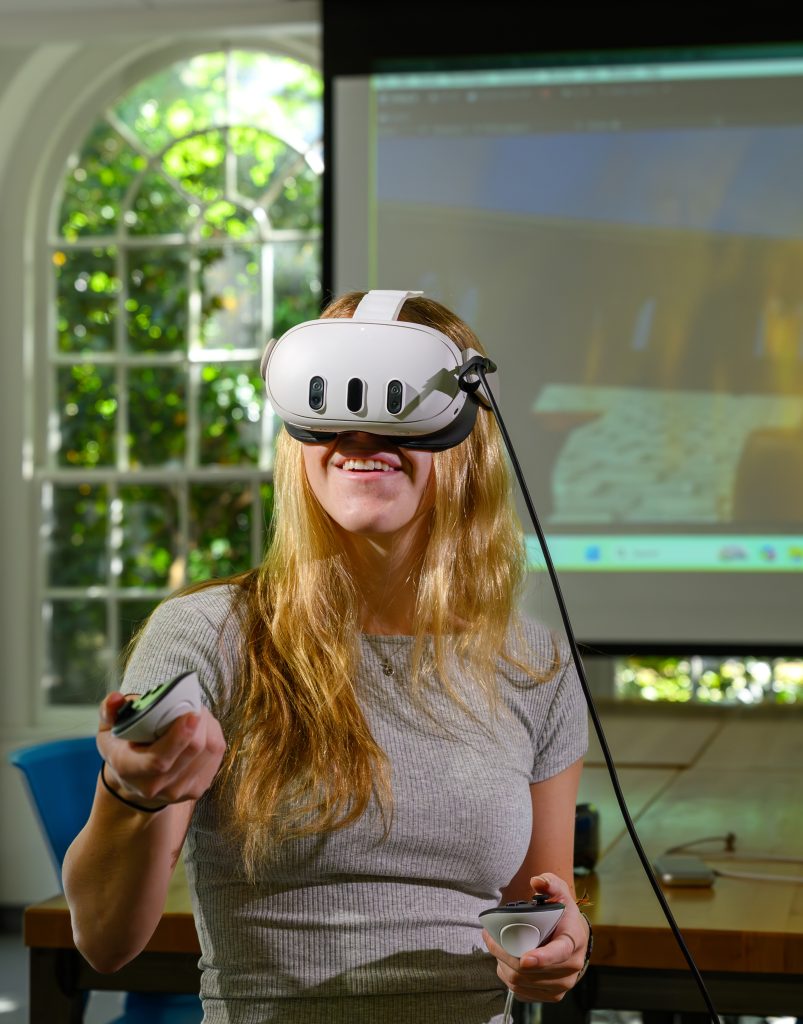 a student wears a virtual reality headset and uses a remote to explore a virtual world
