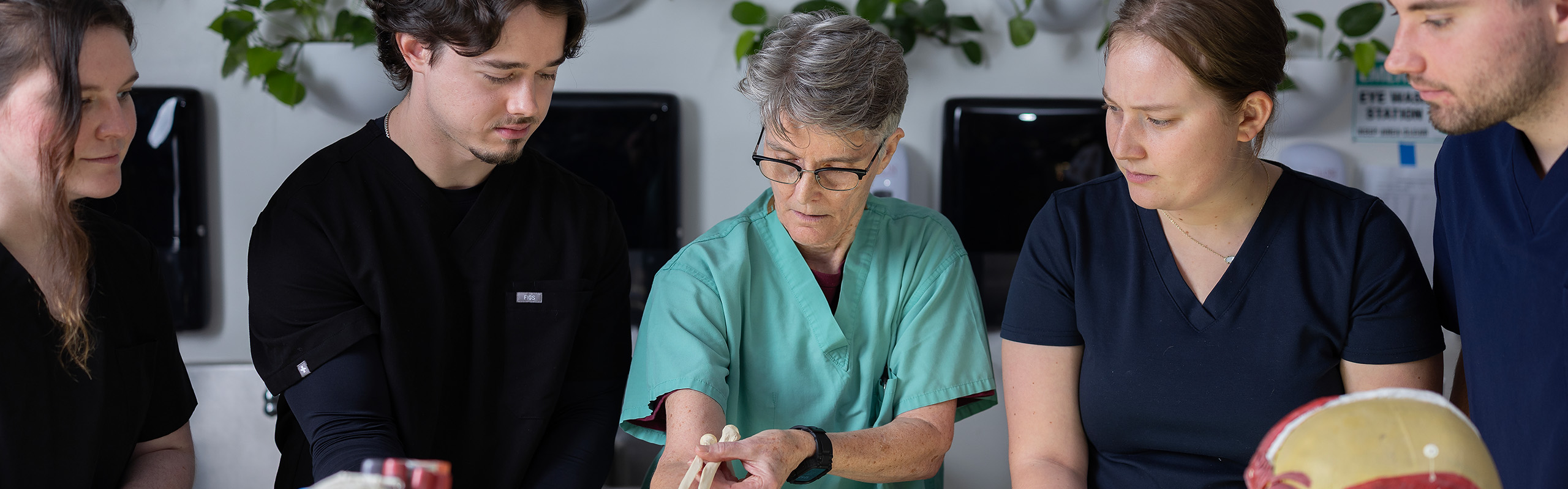 Faculty member guides students as they examine an anatomical joint model during a hands-on lab session.