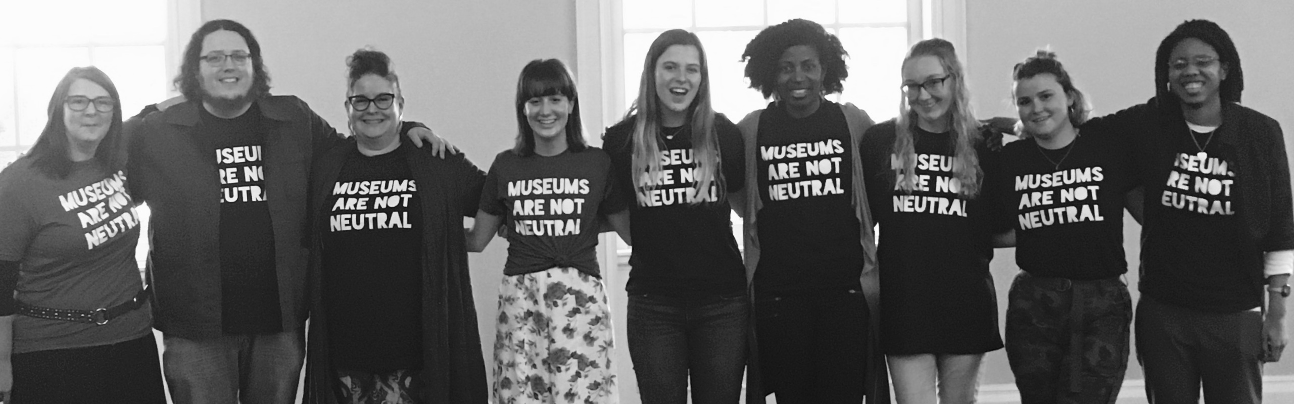 A group of people posing for a photo in a line wearing Museums Are Not Neutral t-shirts