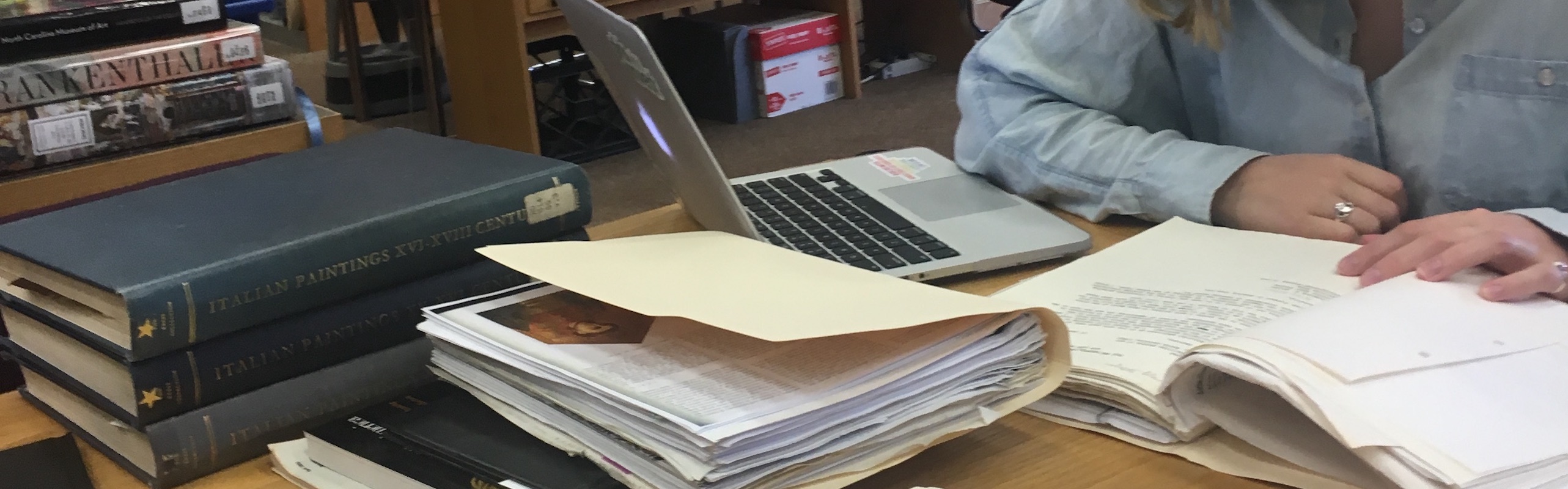 person taking notes from a book and a file folder of pages