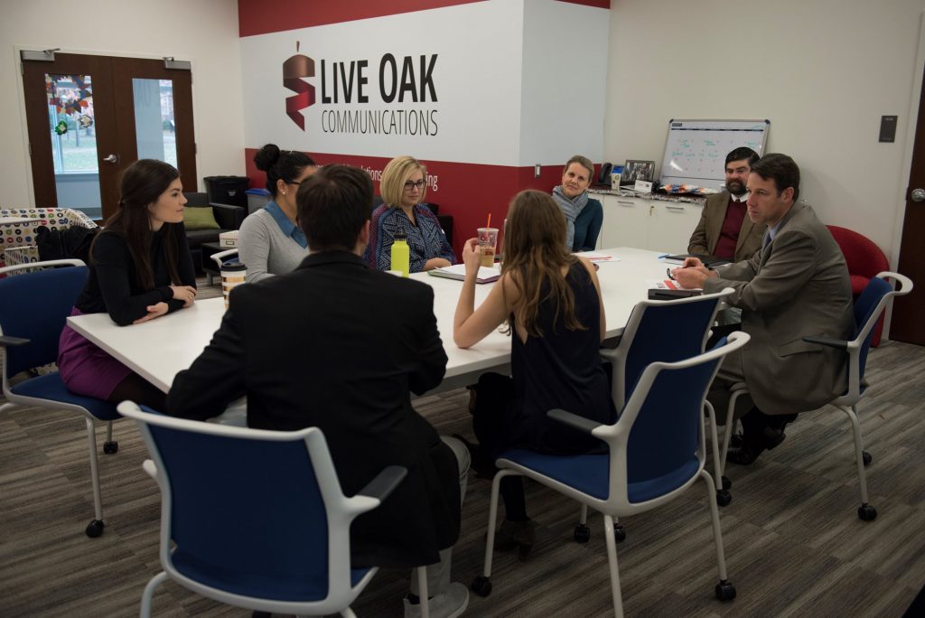 Students and other members of the campus community including Brooke Barnett, Jon Dooley and Hal Vincent, a lecturer in communications and faculty director of Live Oak Communications, meet in the new Live Oak Communications office, situated on the first floor of Schar Hall.