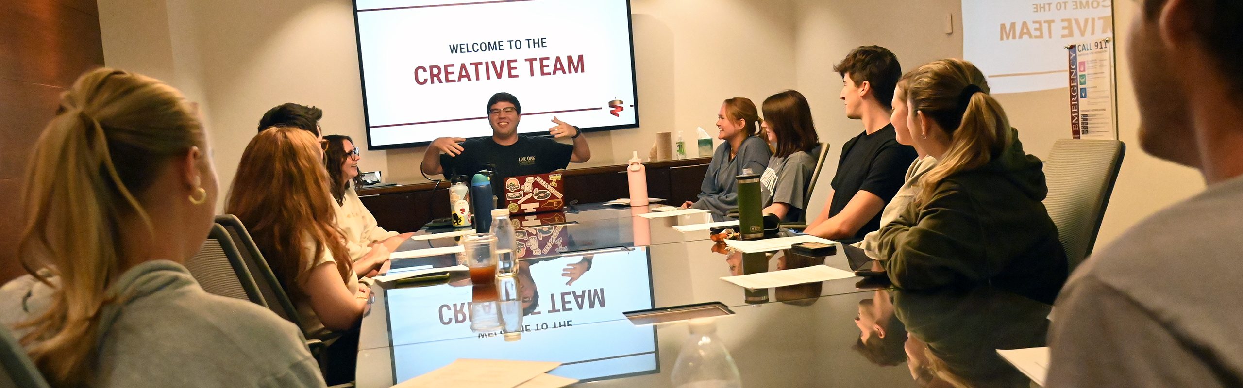 A group of strategic communications majors gather around a table in Schar Hall's conference room discussing upcoming visual communication projects. These students are earning a degree in public relations and advertising.