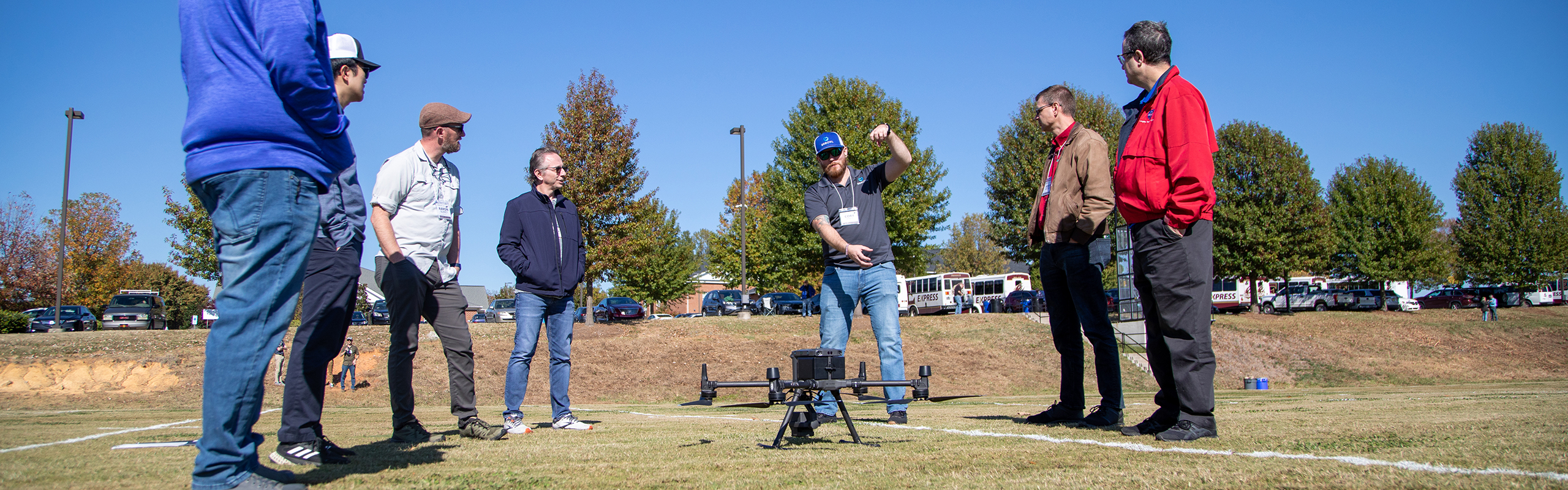 A group of men stand in a circle with a drone nearby.