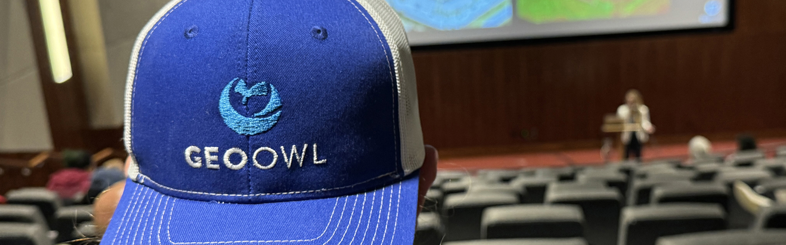 An attendee wears a GeoOwl hat while Kerry Mapes leads a morning presentation.