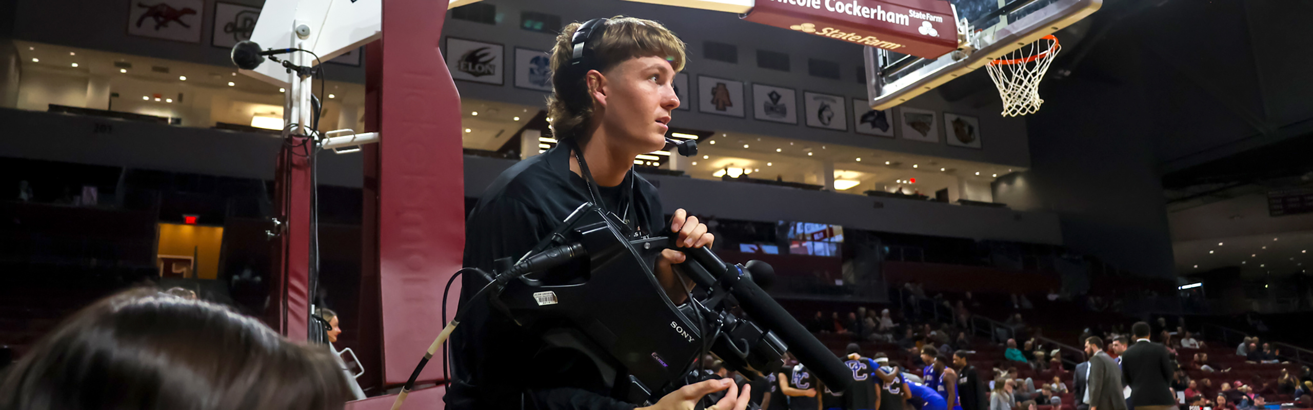 Strickland, enrolled at Elon, one of the best sports broadcasting schools, sits under the basketball goal with a camera in his hands. He is interested in sports broadcasting and sports media,