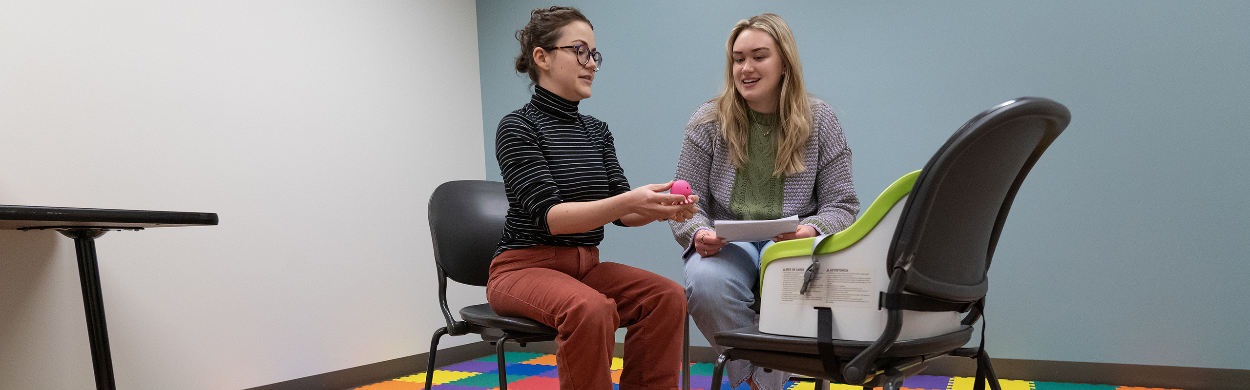 A psychology professor and student research infant development playing with toys. They are seated in chairs around a baby in a carrier. A degree in psychology at Elon prepares your for a wide range of careers and opportunities.