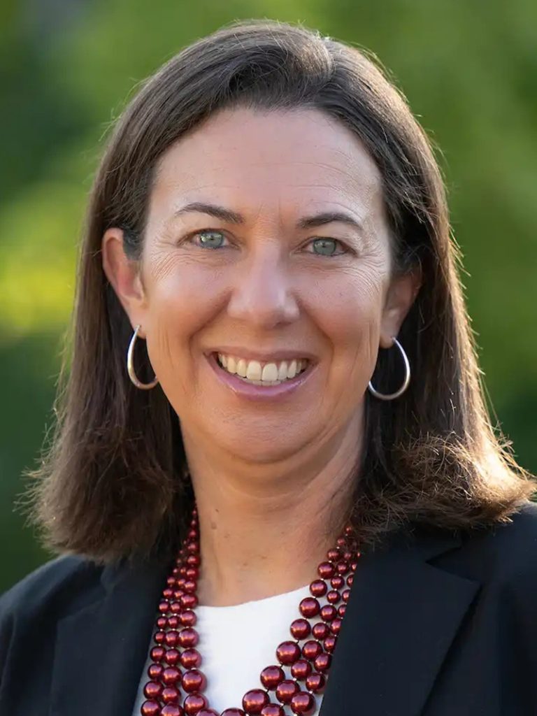 Female athletic director stands for a headshot in front of a green background.