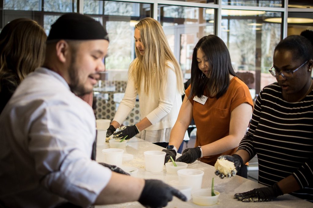 Elon Dining's Chef Danny stands in front of three students as they break down ingredients.