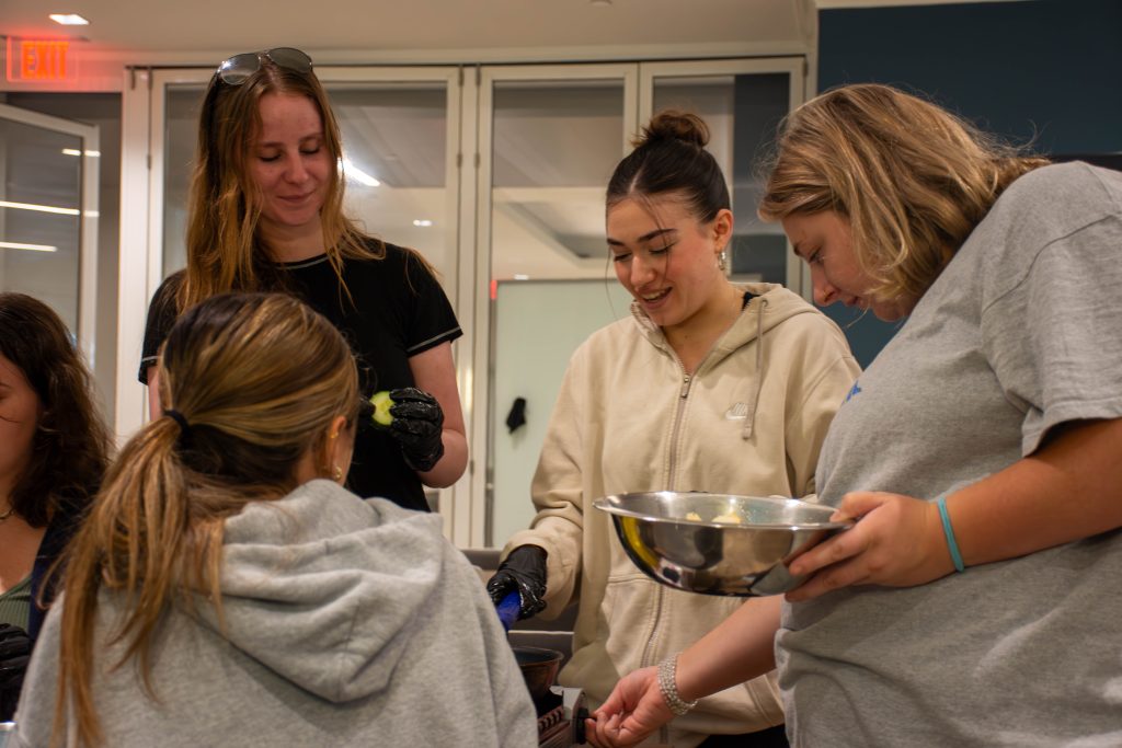 Three students stand around a burner, working together to prepare for a teaching kitchen