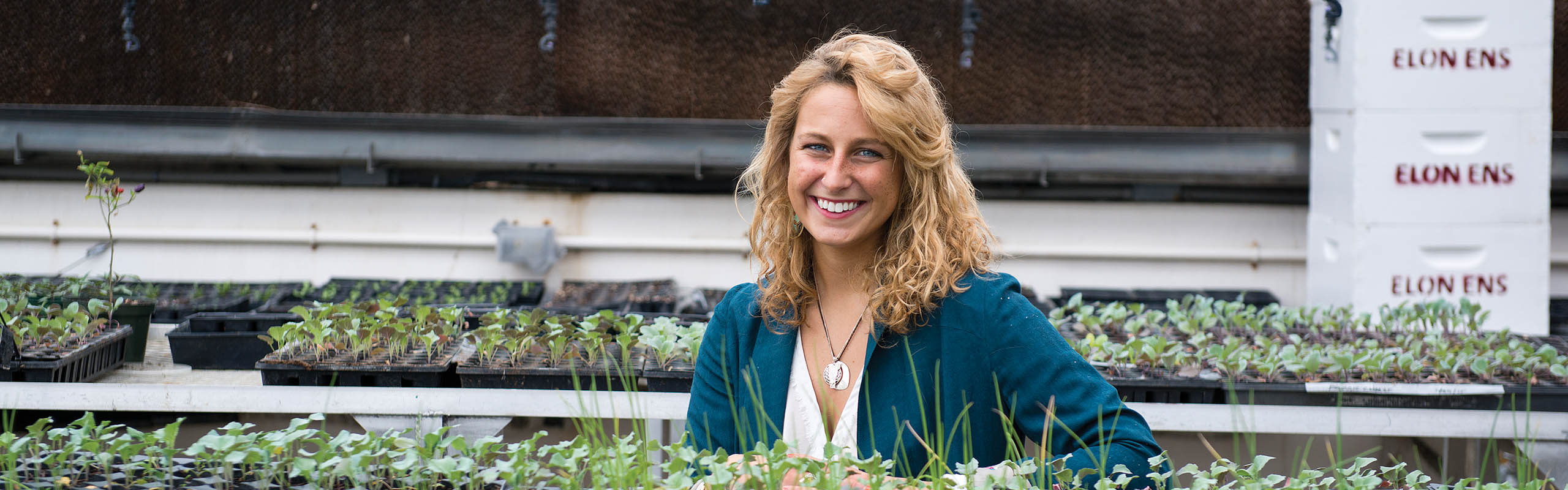 Colby Halligan '15 poses in Elon's greenhouse, with plants that will be sold to raise funds for Elon's Community Garden.
