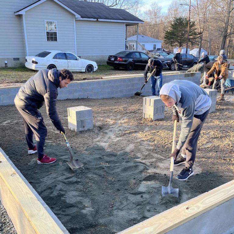 Two students spread concrete at a housing build site.