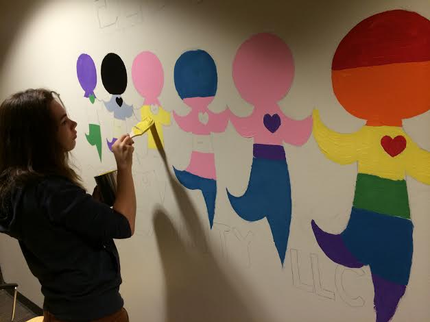 Female student painting on the wall of the Gender & Sexuality Living Learning Community.