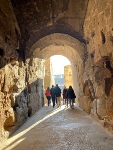 A group of people walking through a stone archway toward a light source.