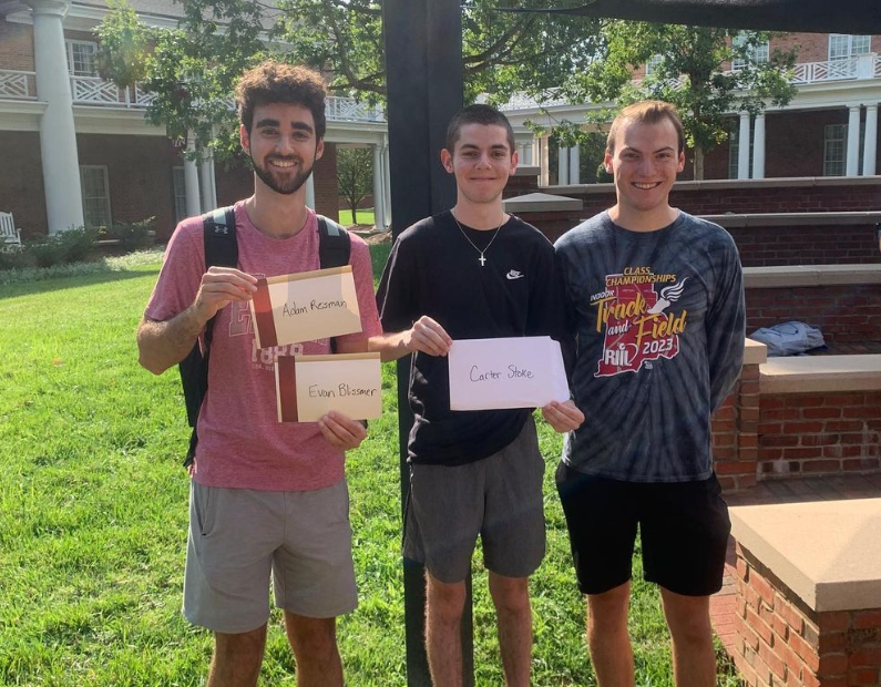 Photo: 3 college students smile at the camera in the grassy quad outside of Billy House. First-years Adam and Evan are matched with their peer mentor, Carter!