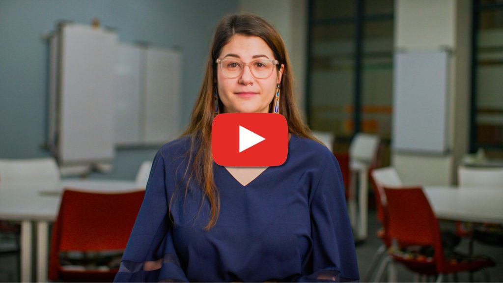 A woman wearing glasses stands in a classroom or learning space, facing the camera. A play button overlay indicates this is a video about the Canvas transition.