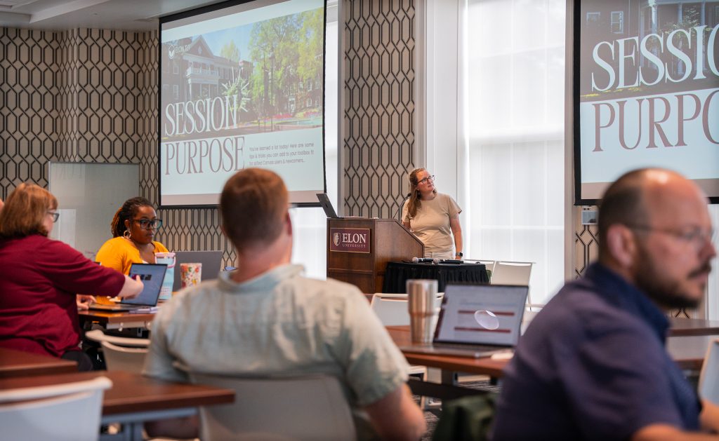 Faculty and staff attend a professional development session in a conference room at ������Ƶ. A presenter stands at a podium beside two large projection screens displaying a slide titled 'Session Purpose,' while participants seated at tables follow along using laptops and notebooks.