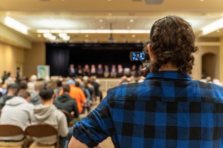 Student stands behind camera filming candidate forum.