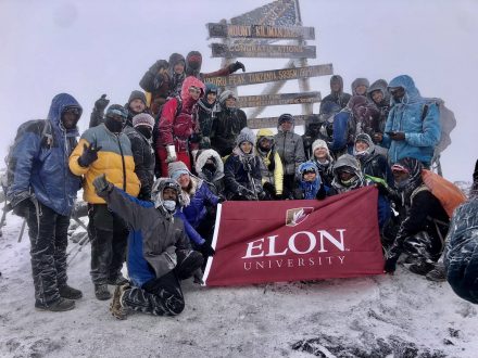 Group of people celebrating at the summit of Mount Kilimanjaro with a Elon University banner.