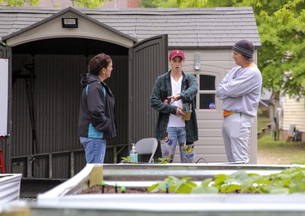 three people standing near raised gardens in front of a shed.