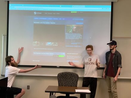 Three students in front of a projection screen showing still images of video games on the Steam website.