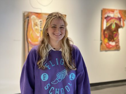 Shelly Freund '22 standing in front of her paintings