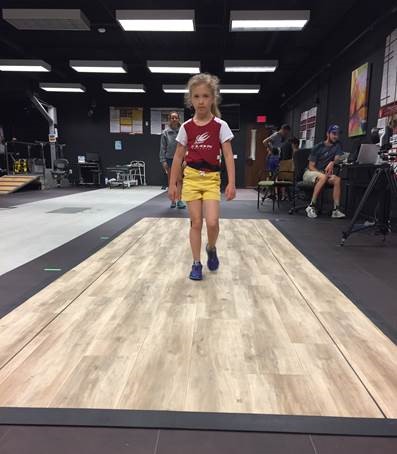 child wearing Elon t-shirt walking toward the camera on a section of wooden floor