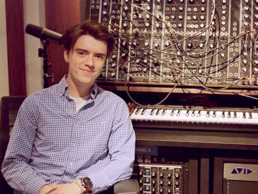 Man facing the camera posed in front of a keyboard and synthesizer.