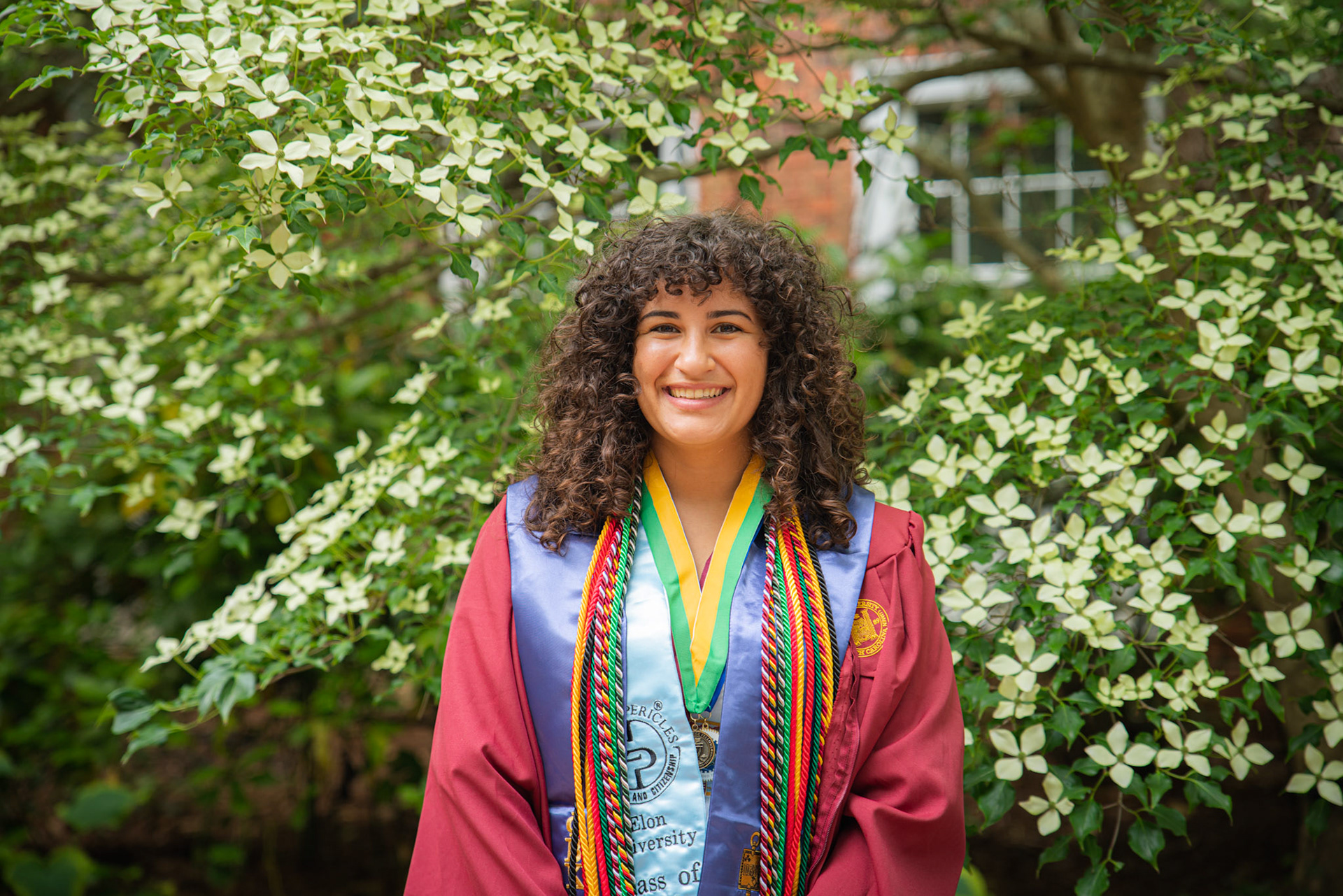 Deena Elrefai in maroon graduation gown with honor cords.