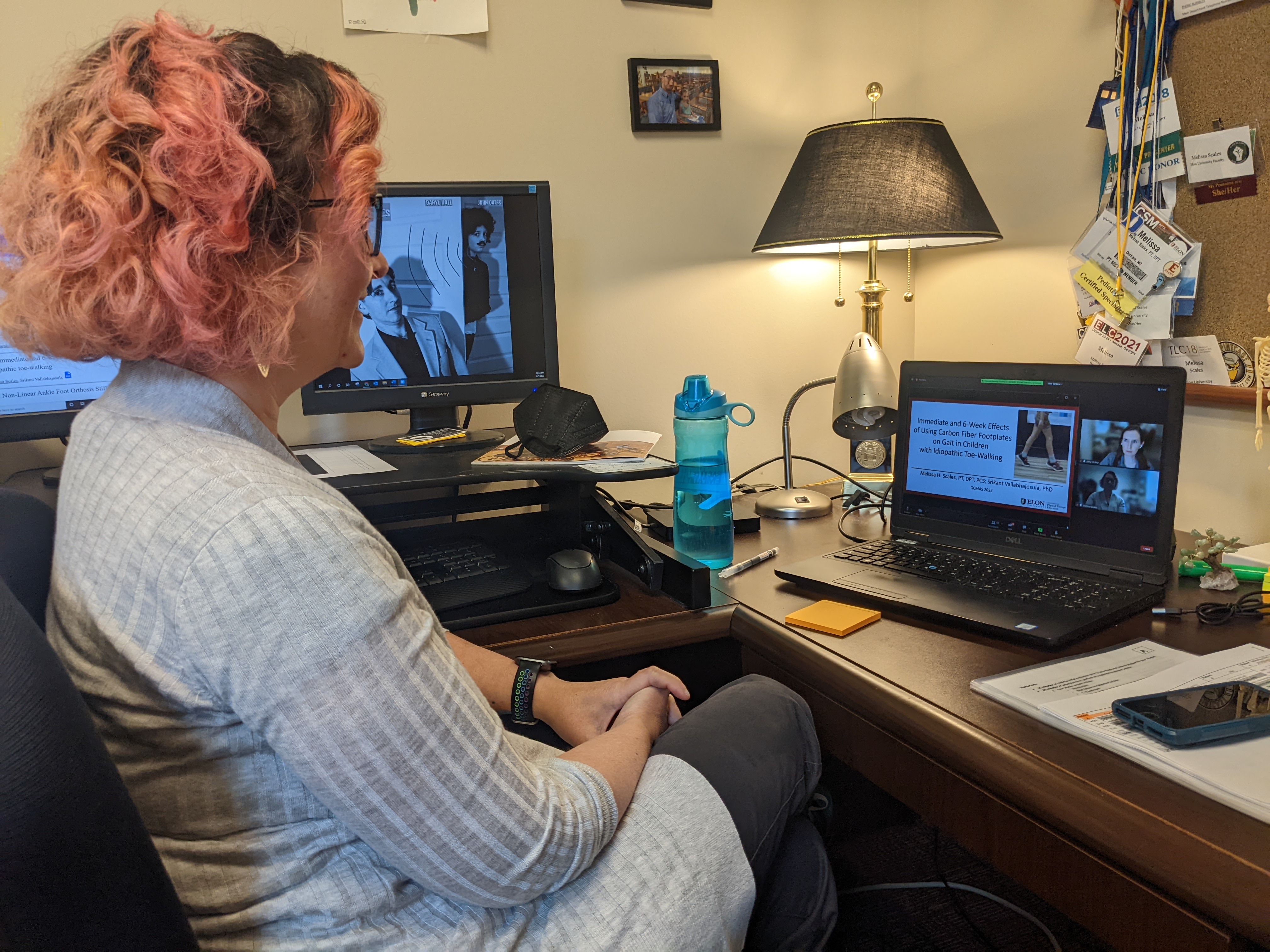 woman with pink curly hair sitting in office chair facing laptop