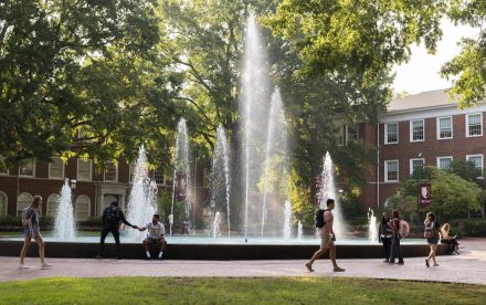 A day view of Fonville Fountain at Elon University surrounded by trees and students walking by it.